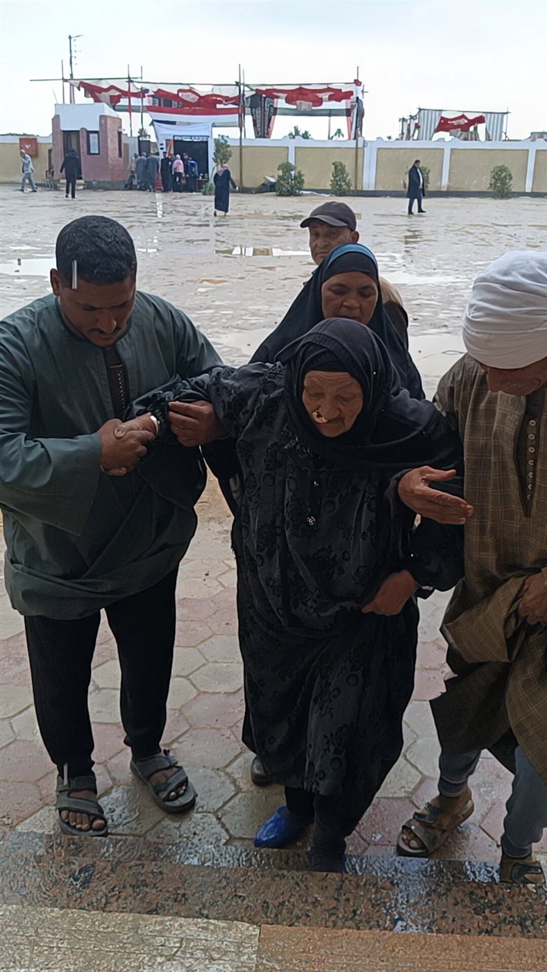 مسنة عمرها 85 عامًا على كرسي متحرك تتحدى المطر للإدلاء بصوتها في لجنة مدرسة اللواء أحمد عبد التواب بطامية