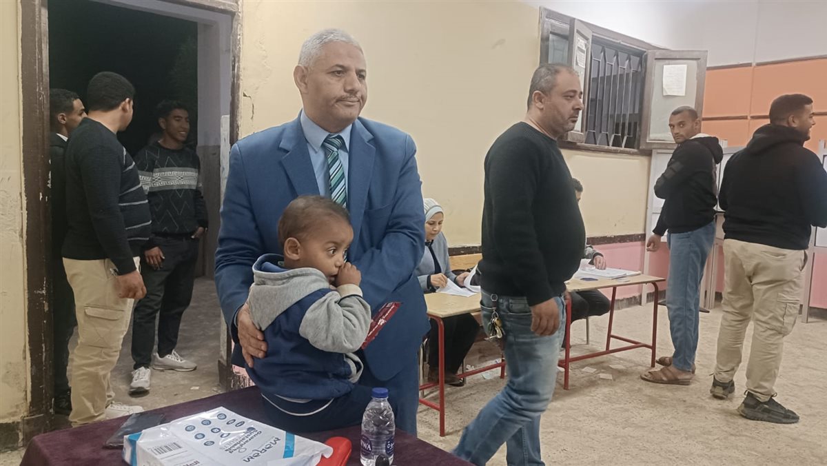 في موقف انساني.. رئيس لجنة في الفيوم يحمل طفل ناخب ليمكن والده من الانتخاب